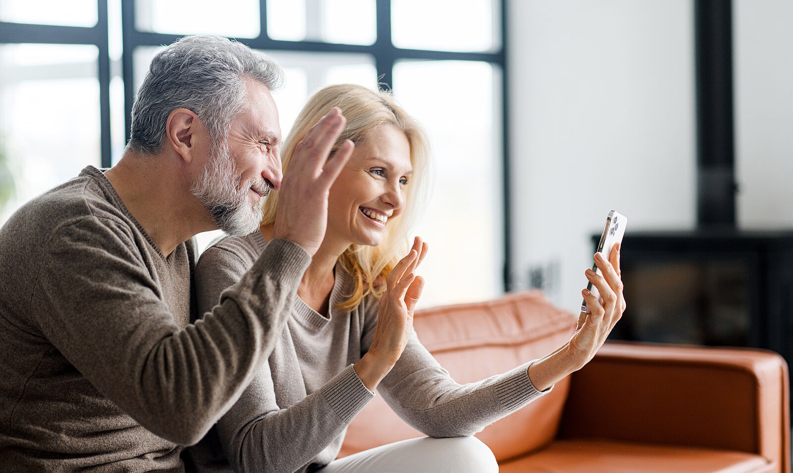 cheerful middle aged couple waving at people on cell phone